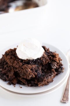 A serving of Oreo Dump Cake with a dollop of whipped cream on top, placed on a white plate next to a fork.
