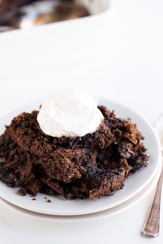 A serving of Oreo Dump Cake with a dollop of whipped cream on top, placed on a white plate next to a fork.