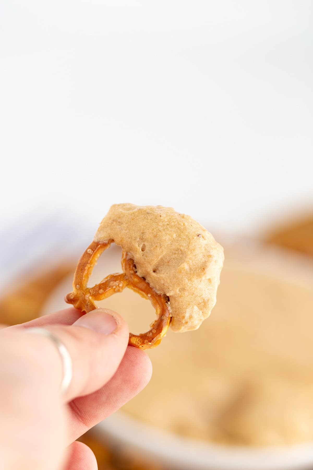 A hand holds a pretzel dipped in a dessert-worthy creamy sauce.