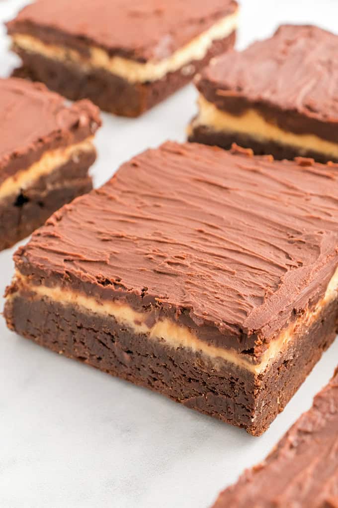 Close-up of buckeye brownies featuring a creamy middle layer sandwiched between chocolatey goodness, topped with rich frosting. Perfectly arranged on a white surface.