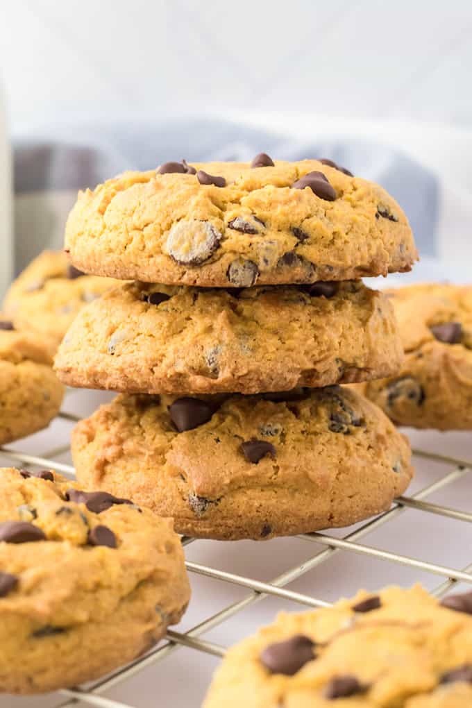 A stack of three cream cheese chocolate chip cookies on a wire rack, surrounded by other deliciously soft cookies.