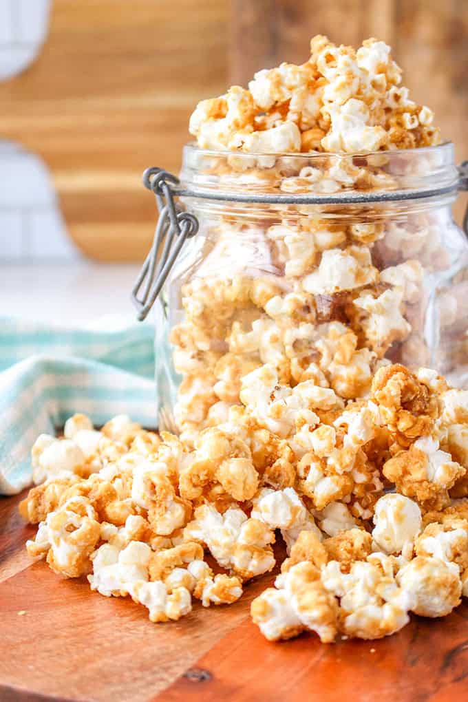 A glass jar filled with old-fashioned caramel corn, with some popcorn spilling out onto a wooden surface.