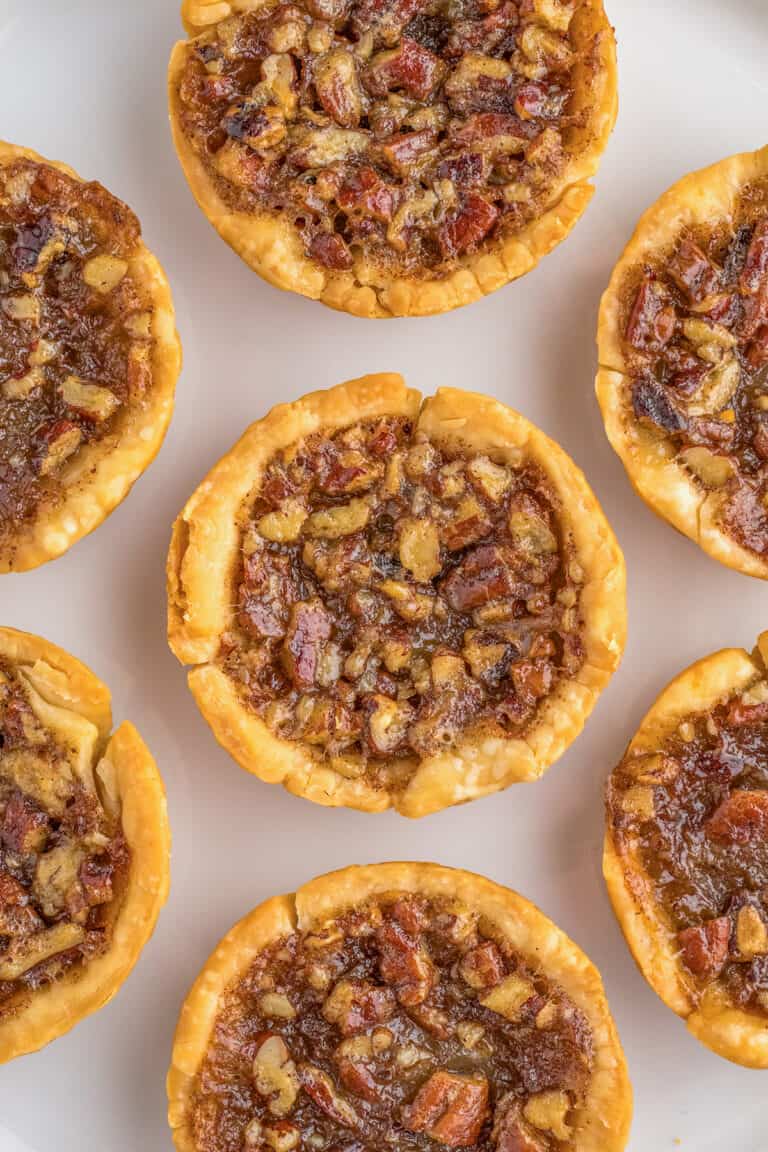 A plate of six mini pecan pies arranged in a circular pattern, featuring a flaky crust and nutty filling.