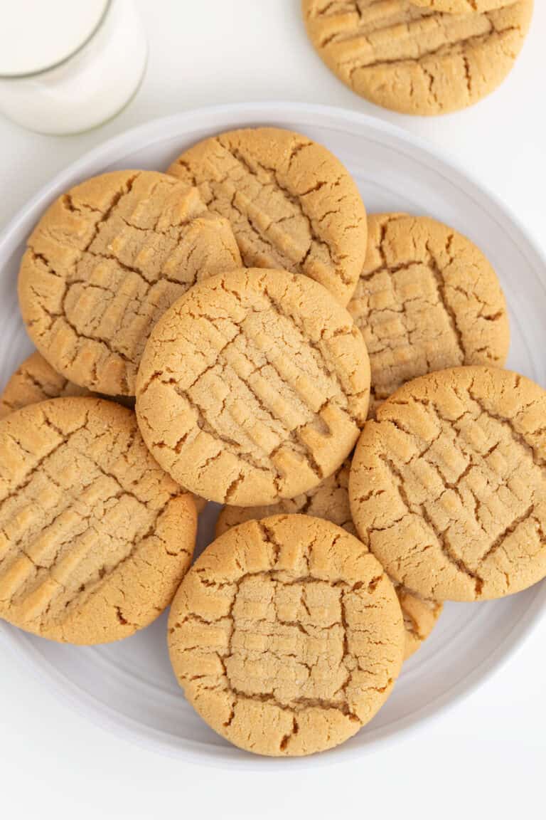 A plate of chewy, crisscross-patterned peanut butter cookies sits invitingly next to a refreshing glass of milk.