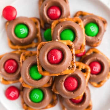 A plate of pretzel squares topped with melted chocolate and red and green M&M candies, each piece beautifully accented by a rich, gooey Rolo.