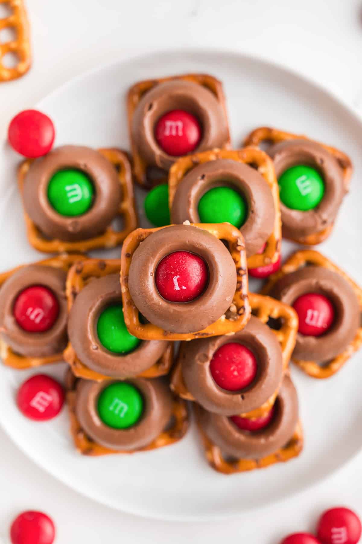 A plate of pretzel squares topped with melted chocolate and red and green M&M candies, each piece beautifully accented by a rich, gooey Rolo.