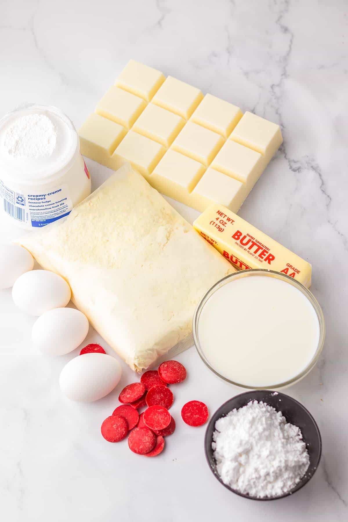 Ingredients for baking on a counter include white chocolate, eggs, a package of mix, milk, red candies, butter, powdered sugar, and a jar of cream—perfect for creating copycat Little Debbie Christmas Tree Cakes.