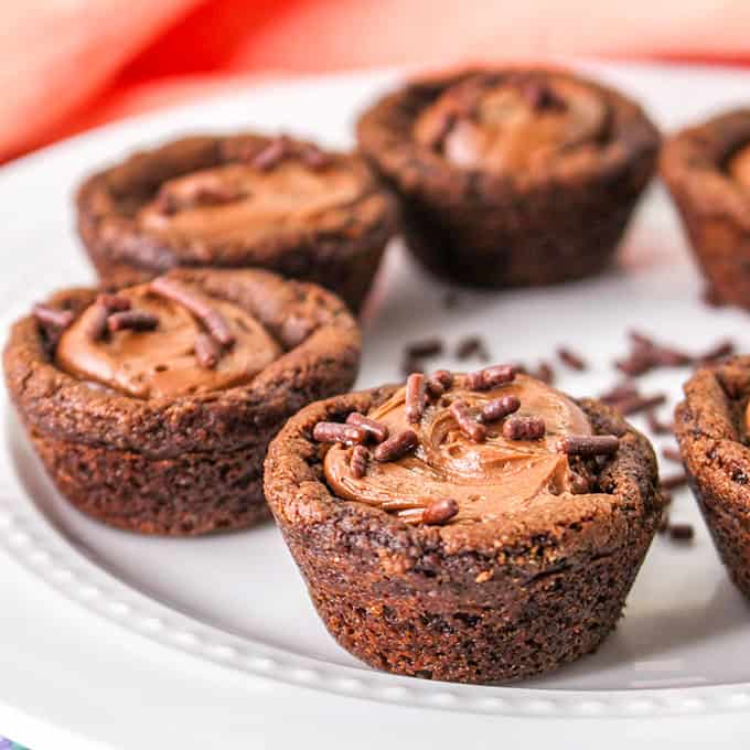 Chocolate cookie cups brimming with rich chocolate frosting and crowned with delicate chocolate sprinkles rest elegantly on a white plate.
