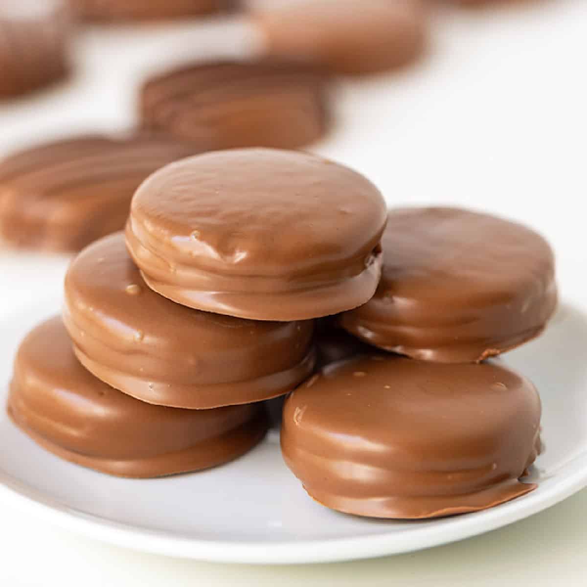 A stack of five chocolate-covered cookies on a white plate, with more Oreos blurred in the background.