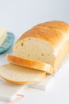 A loaf of sliced potato bread sits elegantly on a marble board, with a blurred butter dish providing a soft backdrop.