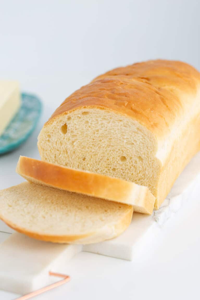 A loaf of sliced potato bread sits elegantly on a marble board, with a blurred butter dish providing a soft backdrop.