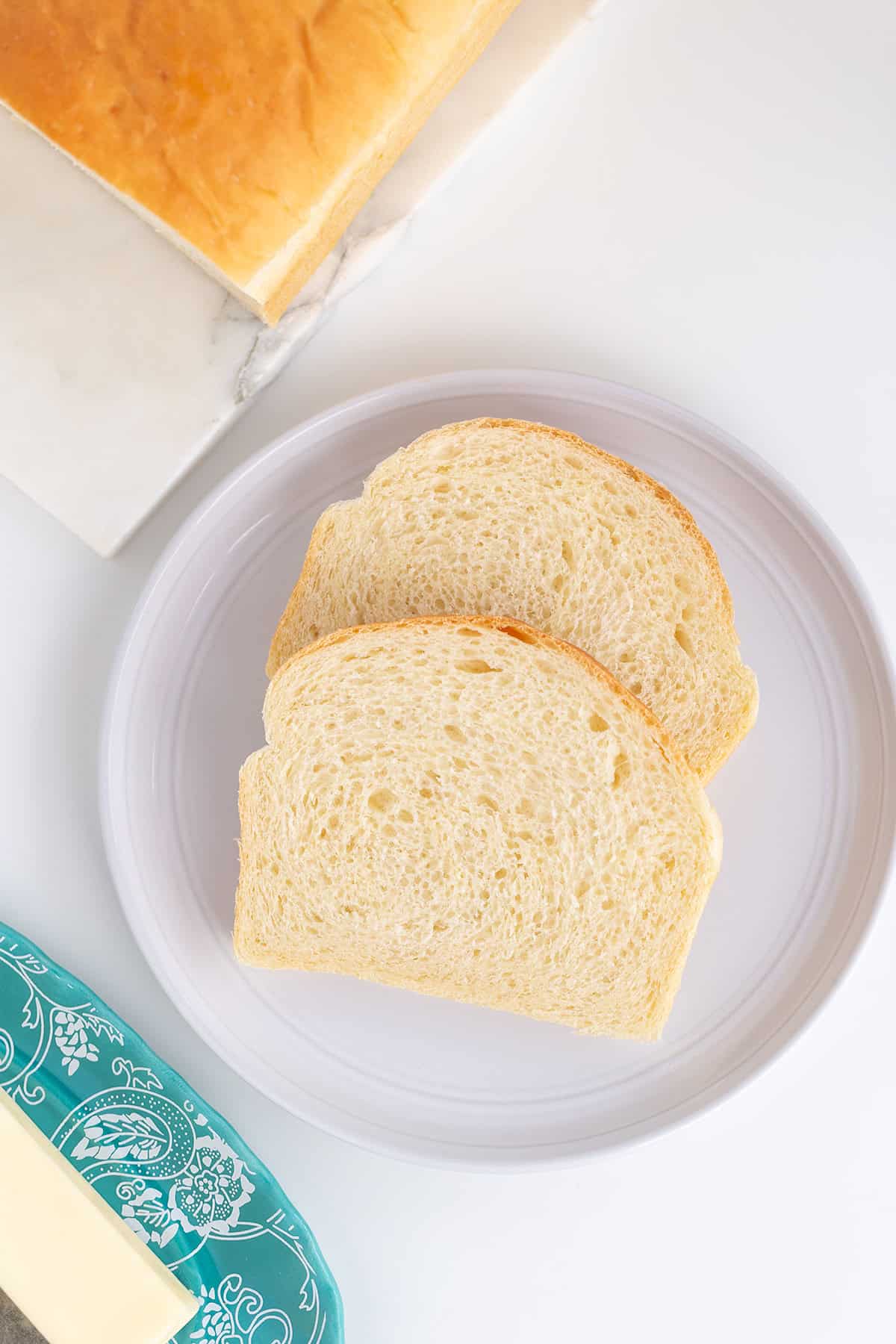 Two slices of potato bread rest on a white plate with a loaf nearby, while a turquoise butter dish sits in the corner.