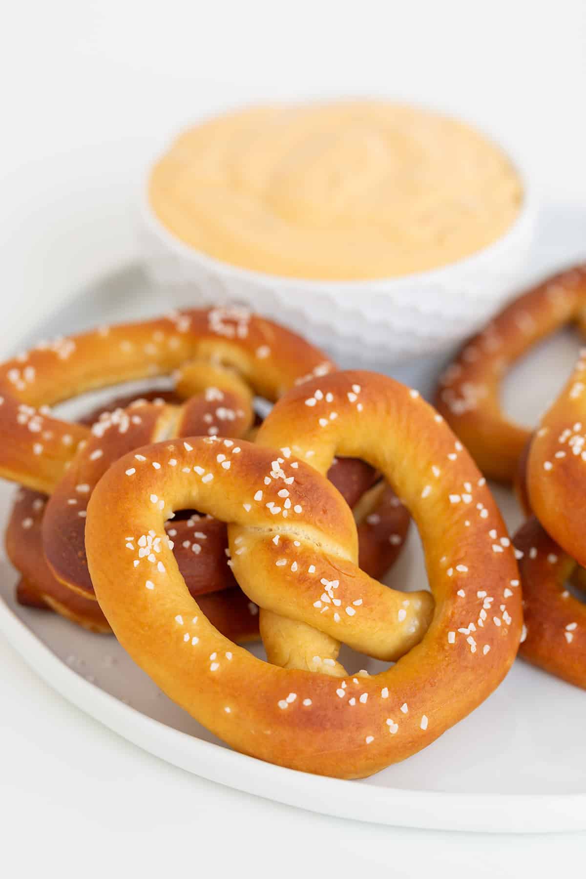 A plate with homemade salted pretzels next to a bowl of creamy cheese dip.