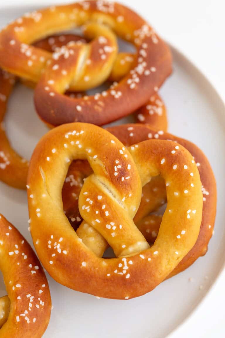 Close-up of homemade soft pretzels, perfectly baked and topped with coarse salt, resting invitingly on a white plate.