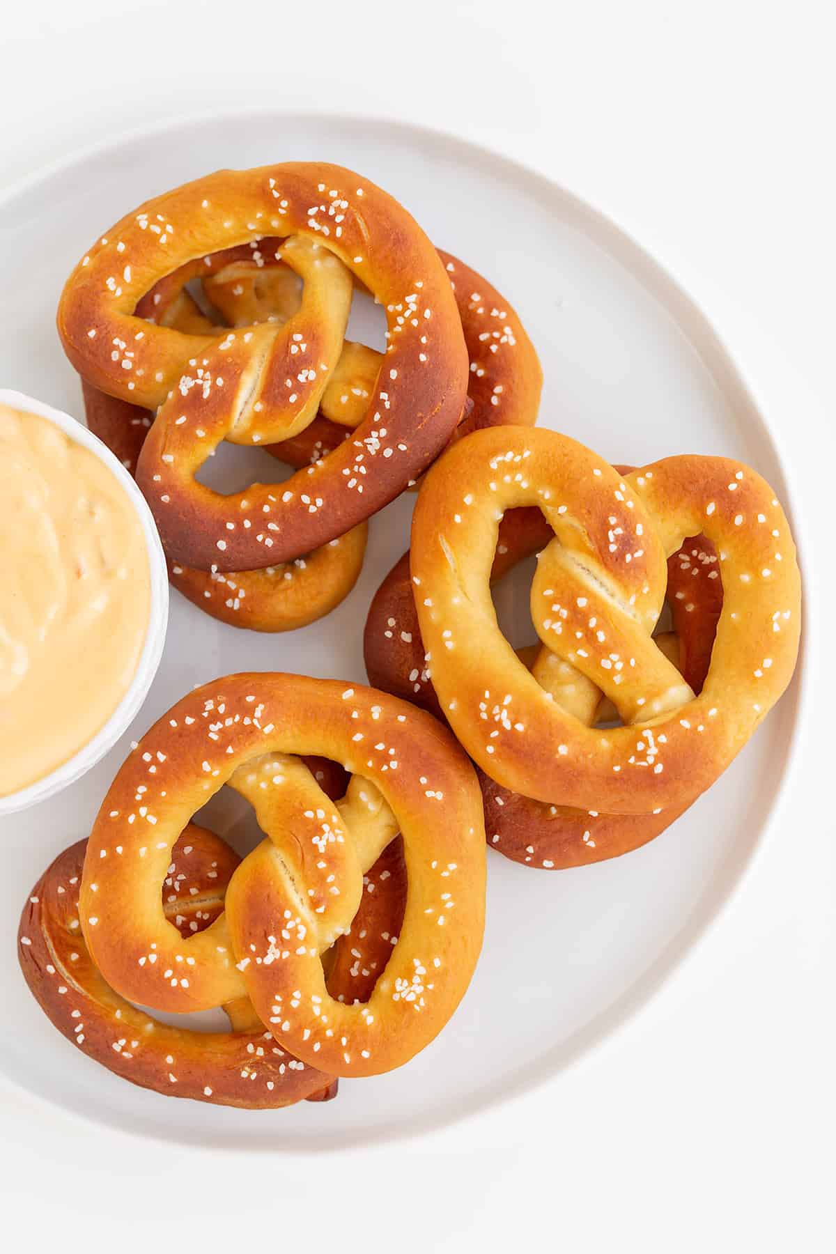 Plate with three homemade soft pretzels and a bowl of cheese dip.