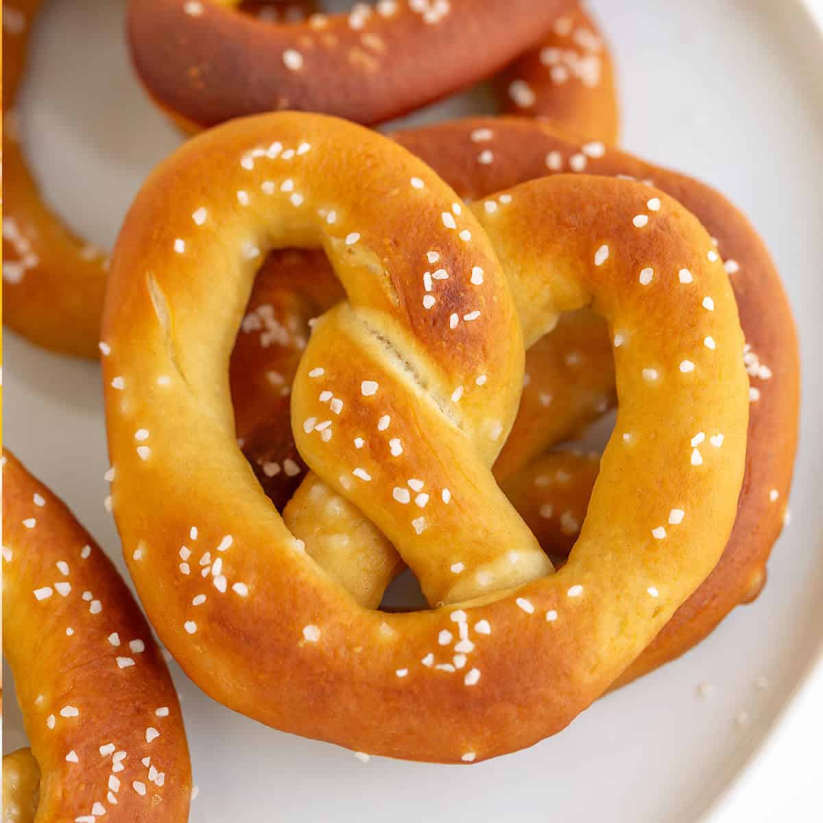A close-up of golden brown homemade pretzels sprinkled with coarse salt on a white plate.