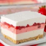 A slice of dessert lasagna with a crumbly base, white and pink creamy layers, and a luscious strawberry topping, served elegantly on a white plate.