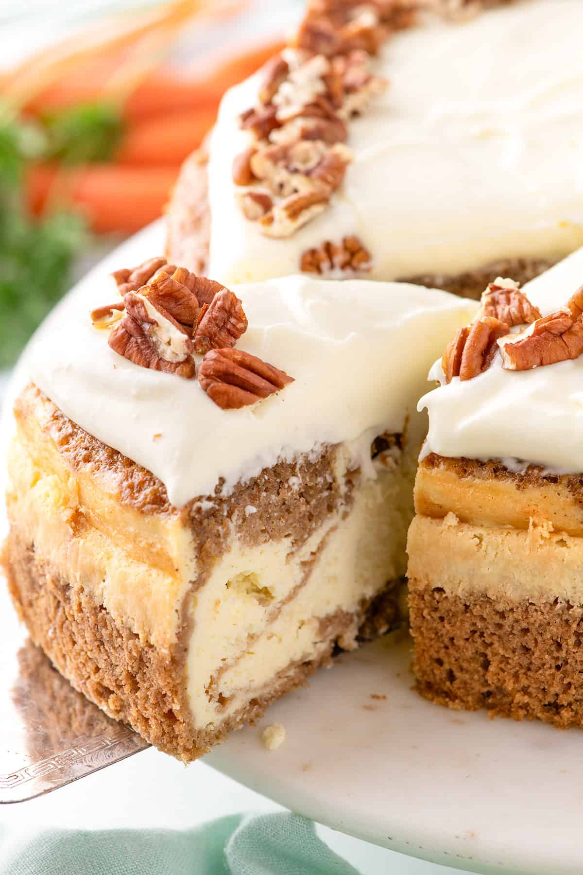 A slice of cream-topped cheesecake with pecan pieces and a marbled interior reminiscent of a rich carrot cake sits on a plate.