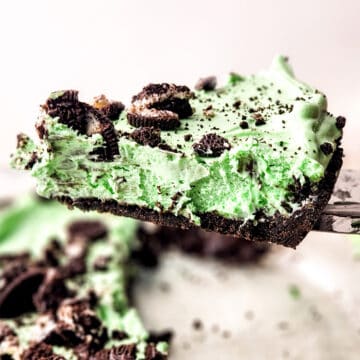 Slice of mint chocolate pie with crushed cookies on top, being lifted from a glass pie dish.