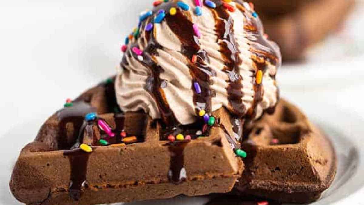 A chocolate waffle crafted from cake mix, topped with a scoop of ice cream, chocolate syrup, and multicolored sprinkles on a white plate.