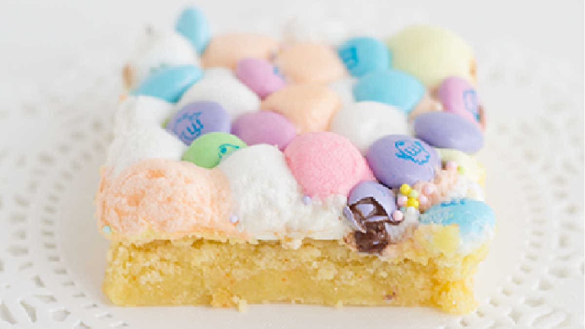 A dessert bar crafted from a yellow cake mix, adorned with colorful marshmallows and candy-coated chocolates, elegantly presented on a white lace doily.