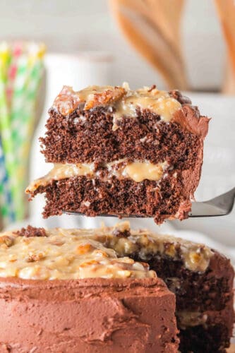 A slice of layered German Chocolate Cake with creamy filling and frosting is lifted from the whole cake, showcasing its rich texture and decadent layers.