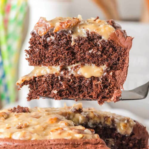 A slice of layered German Chocolate Cake with creamy filling and frosting is lifted from the whole cake, showcasing its rich texture and decadent layers.