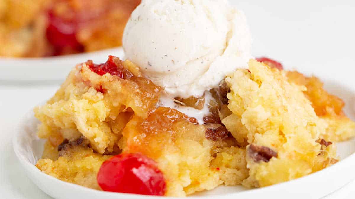 A serving of pineapple upside-down cake, made with a delightful cake mix, features cherries and is topped with a scoop of vanilla ice cream on a white plate.