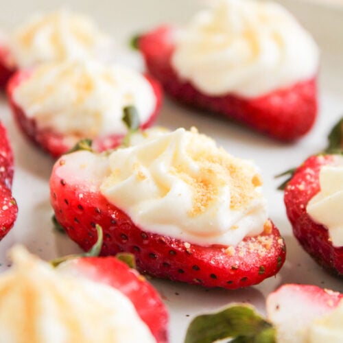 Halved strawberries filled with a swirl of cheesecake cream and sprinkled with crumbs are arranged on a white surface, creating a delightful deviled strawberries dessert.