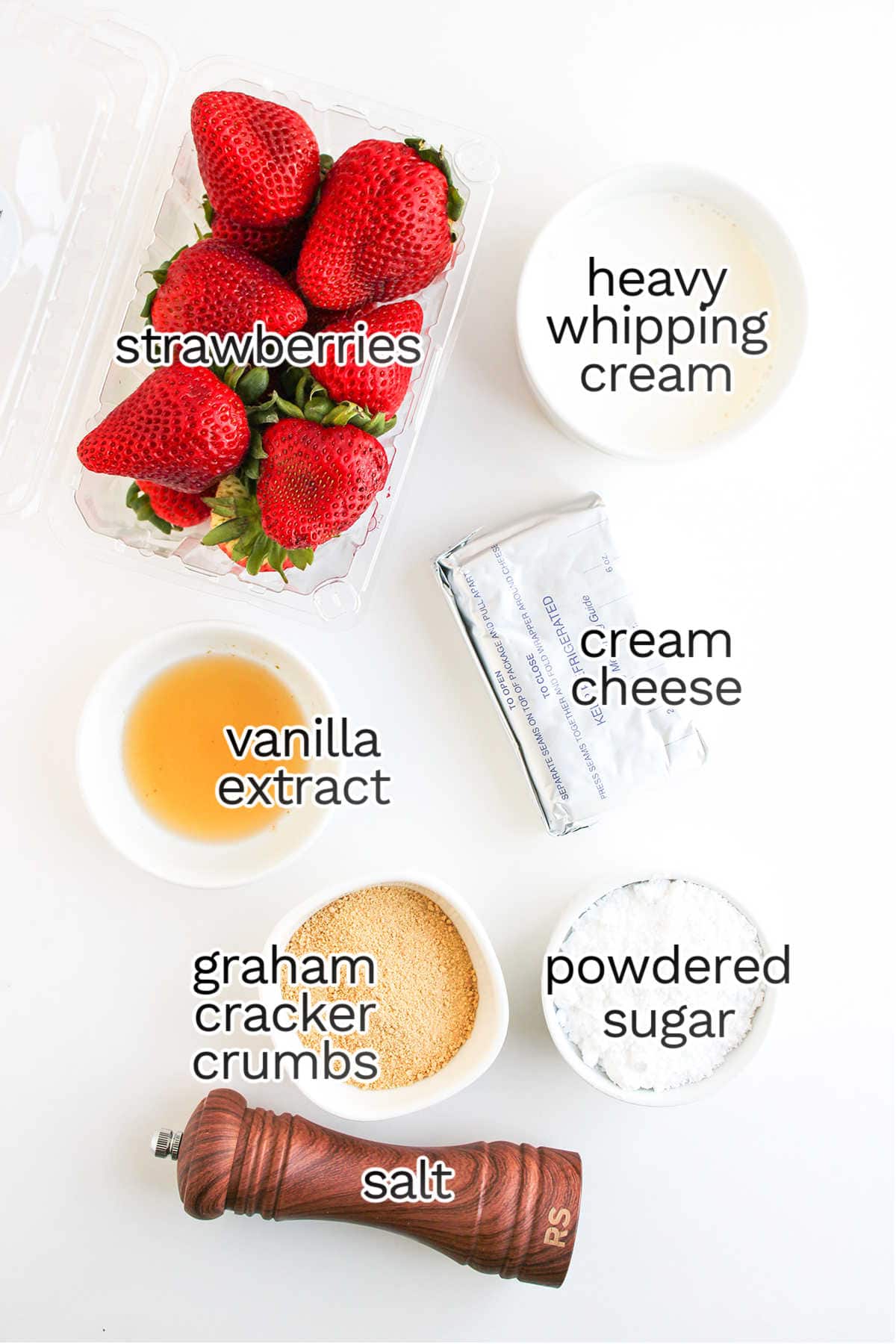 Top-down view of ingredients for Deviled Strawberries: strawberries, heavy whipping cream, cream cheese, vanilla extract, graham cracker crumbs, powdered sugar, and salt—a delicious dessert with classic cheesecake flavors.