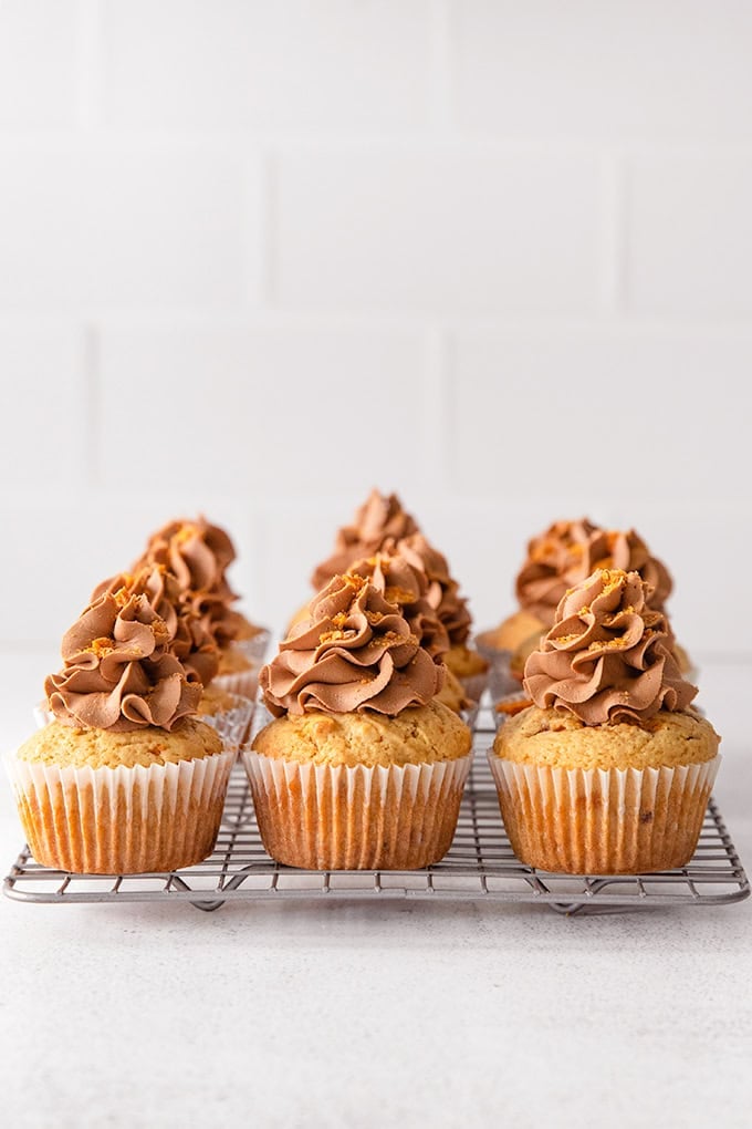 Eight peanut butter cupcakes with chocolate frosting are arranged on a cooling rack against a white tiled background.
