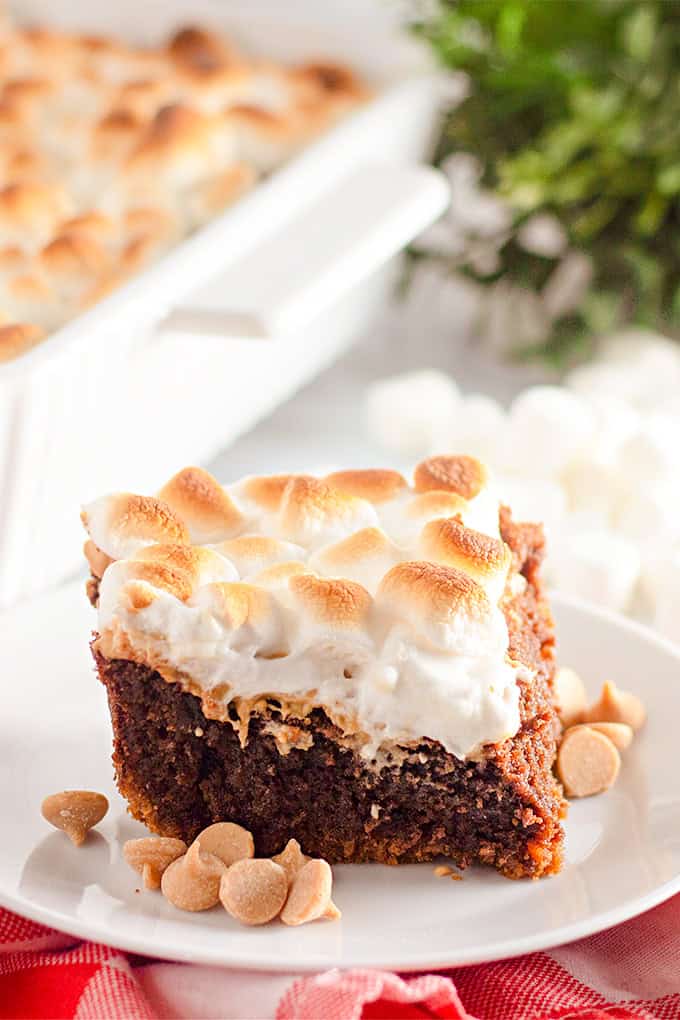 Des tranches carrées de beurre d'arachide sont au sommet de brownies s'mores, à guimauve tossé, se trouve sur une assiette blanche, avec des copeaux de beurre d'arachide éparpillés à proximité.