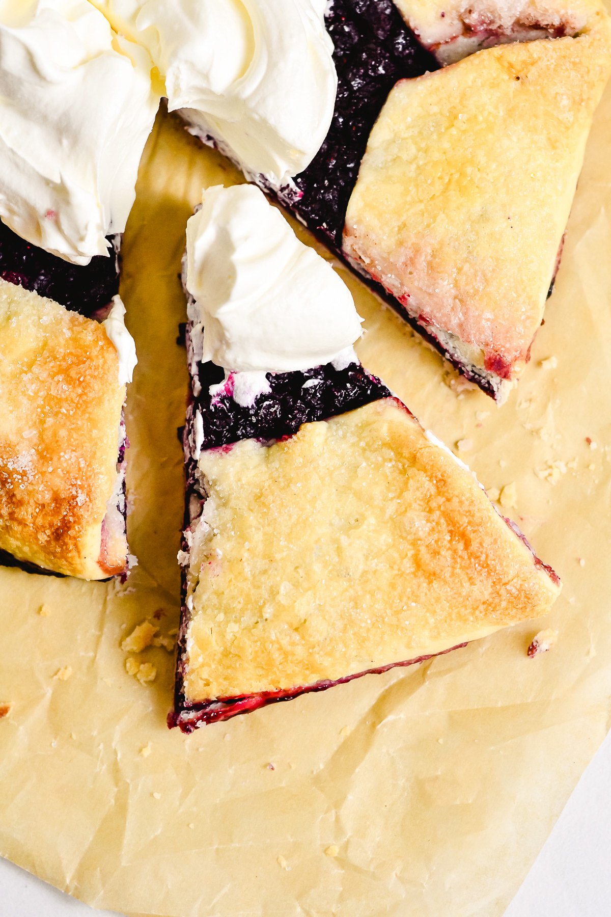 A sliced blueberry galette topped with dollops of whipped cream sits on parchment paper, showcasing the perfect rustic pie for any blueberry dessert lover.