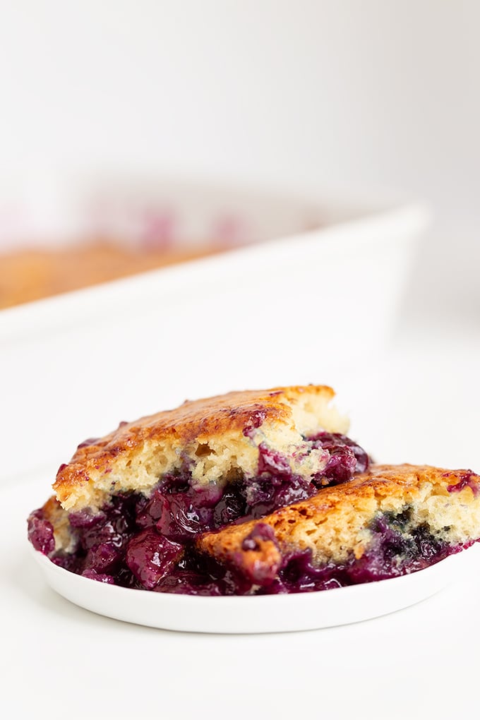 A serving of Easy Blueberry Cobbler with a golden-brown biscuit topping and juicy blueberry filling is presented on a white plate.