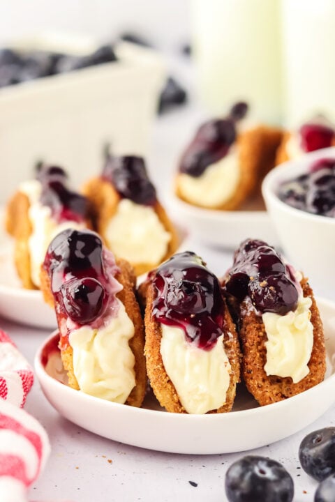 blueberry cheesecake tacos on a small white rimmed plate with blueberries scattered around and a red and white striped linen next to the plate