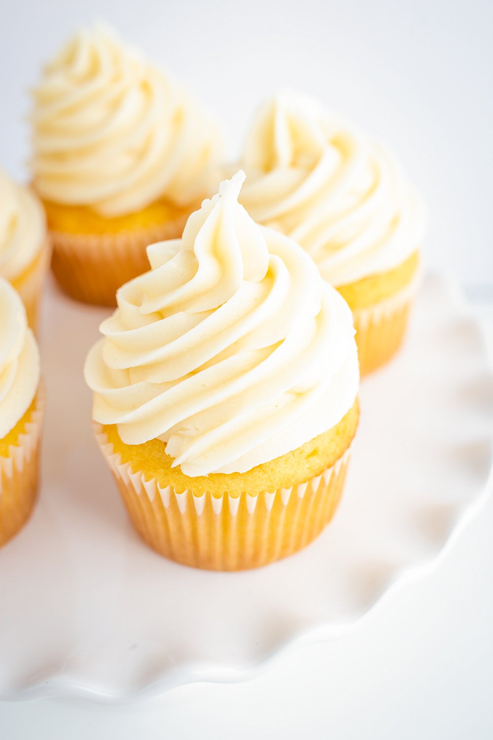 cupcakes with tall frosting swirls on a white ruffle edge cake plate