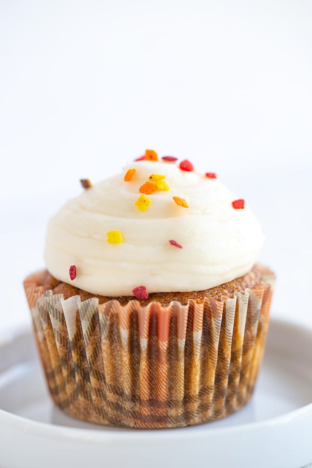 pumpkin cupcake in a fall flannel cupcake liner with cream cheese frosting and fall leaf sprinkles on it on a plate with a small lip