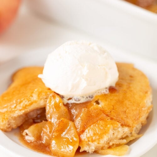 A serving of apple cobbler with visible apple slices, reminiscent of classic apple cobbler, topped with a scoop of vanilla ice cream on a white plate.