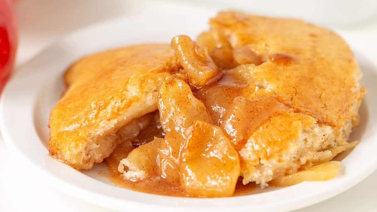 A serving of apple cobbler with cinnamon-spiced apple filling and golden biscuit topping on a white plate—an inviting classic among autumn desserts.