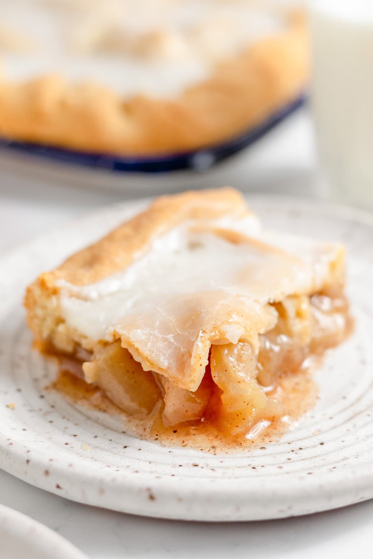 A slice of Apple Slab Pie with a golden crust and visible apple filling sits on a white speckled plate.