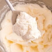 A metal spoon holds a scoop of creamy, whipped marshmallow frosting above a mixing bowl filled with more easy frosting.