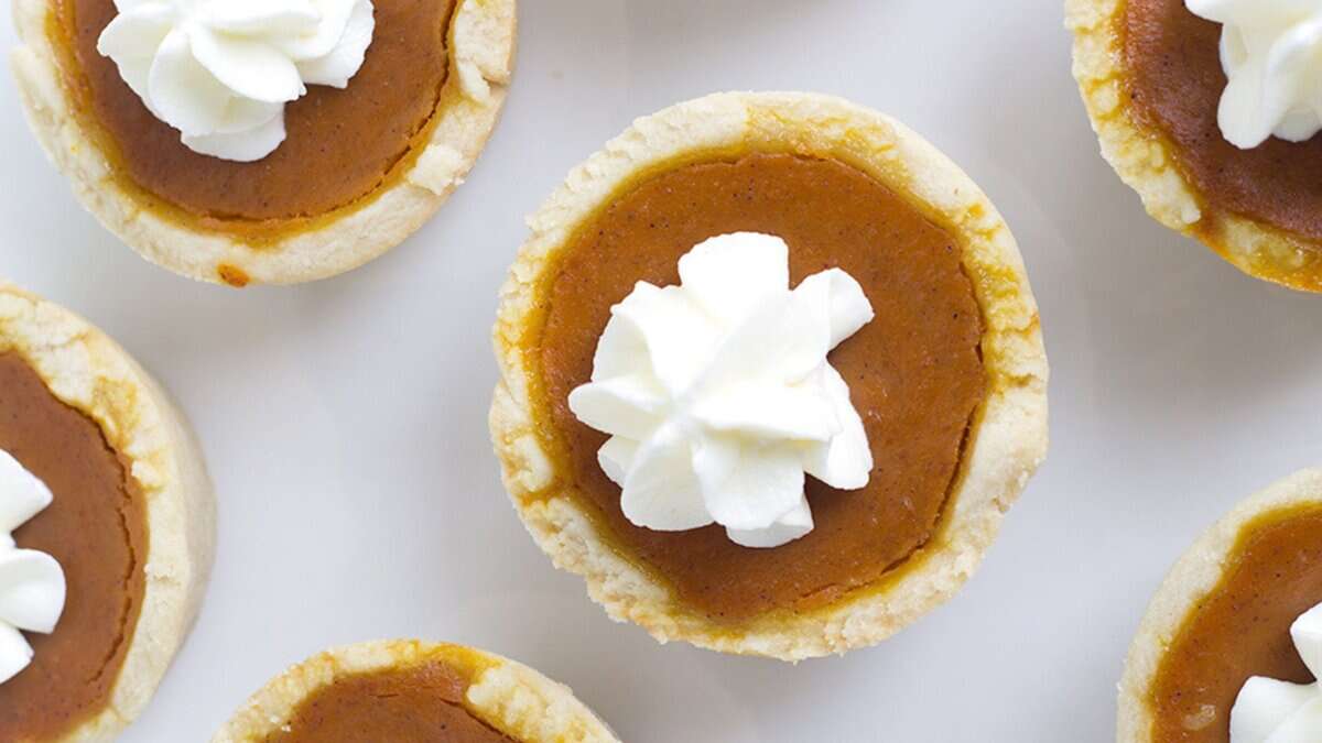 Mini pumpkin pies with a dollop of whipped cream on top, arranged on a white surface—perfect for Autumn Desserts and cozy Seasonal Sweets.