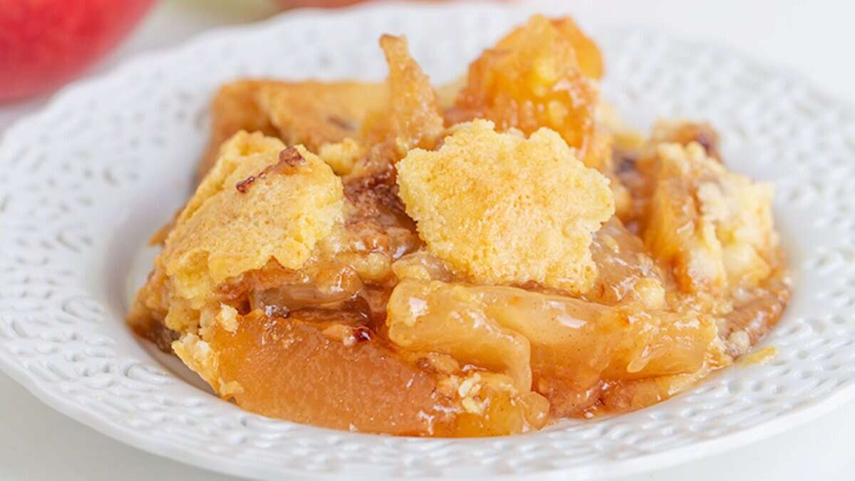A serving of peach cobbler with a golden, crumbly topping sits on a white plate—one of the coziest Autumn desserts.