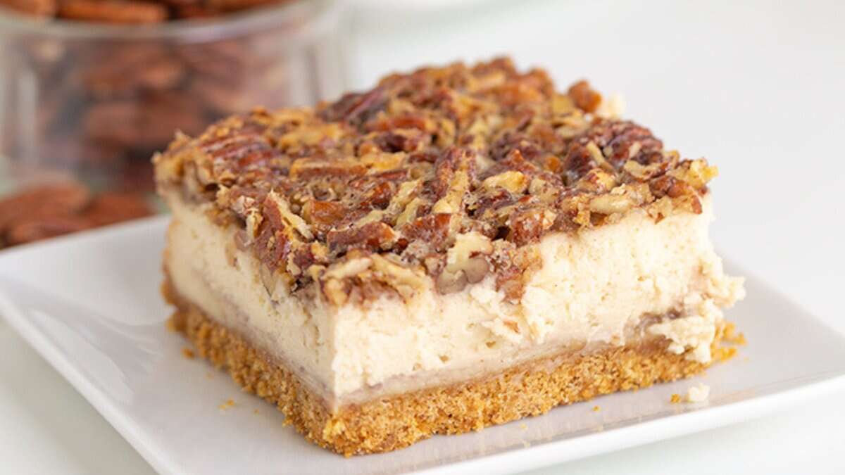 A slice of pecan-topped cheesecake with a graham cracker crust on a white plate—perfect for fans of Autumn desserts and cozy fall recipes.