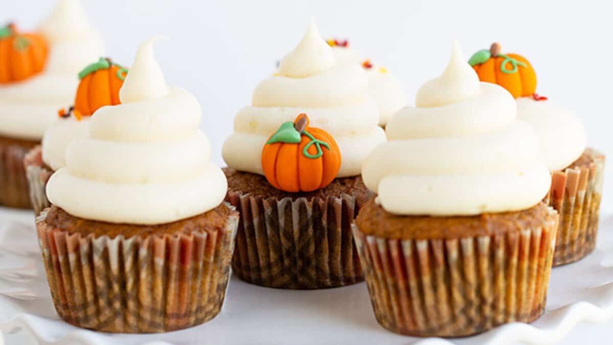 Pumpkin cupcakes topped with swirls of white frosting and pumpkin-shaped fondant decorations make the perfect autumn dessert for your collection of seasonal sweets.