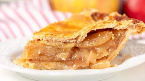 A close-up of a slice of apple pie with a golden, flaky crust on a white plate—perfect for fans of classic fall desserts.