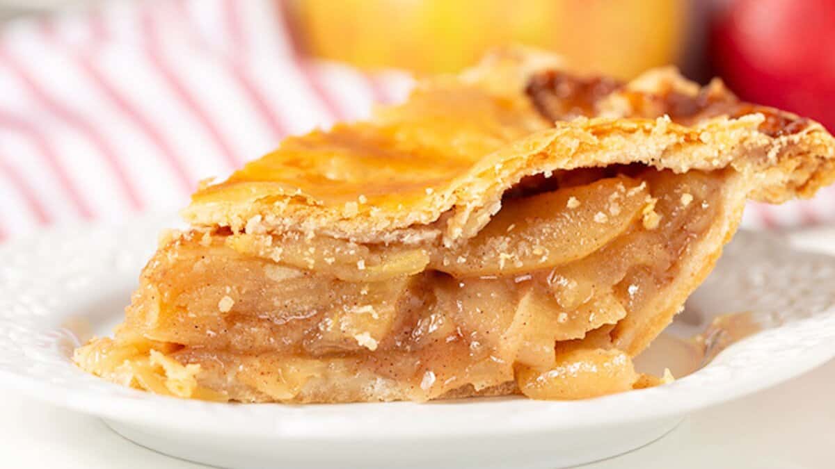 A close-up of a slice of apple pie with a golden, flaky crust on a white plate—perfect for fans of classic fall desserts.