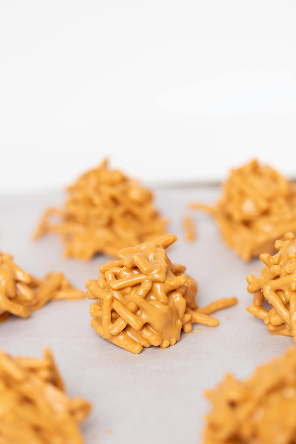 Clusters of chow mein noodles coated in a rich butterscotch mixture create classic Butterscotch Haystacks, arranged on parchment paper for easy, no bake treats.