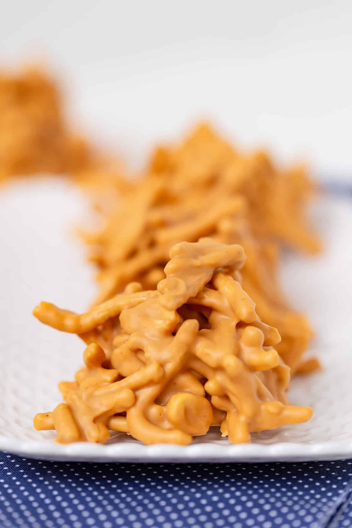 Close-up of No Bake Butterscotch Haystacks cookies arranged on a white textured plate, with a blurred background.