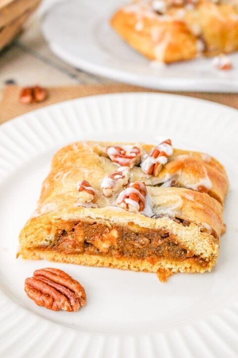 A slice of pecan braid pastry filled with a brown pecan mixture, topped with icing and whole pecans, on a white plate.
